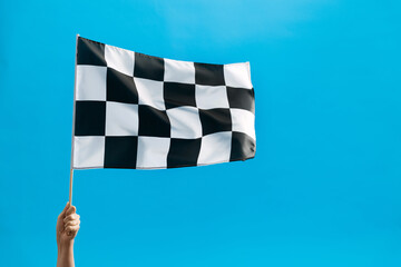 Human hand waving checkered flag on blue background