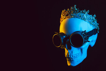 human skull in a crown and steampunk glasses with colored yellow blue neon light on a black background
