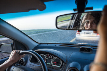 Latin woman driving a car on the route while adjusting the rear view mirror. Copy space.
