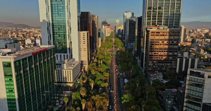 Mexico City Aerial v9 drone flying straight over paseo de la reforma between downtown high rise buildings and towers capturing urban cityscape at sunset - Shot with Mavic 3 Cine - December 2021