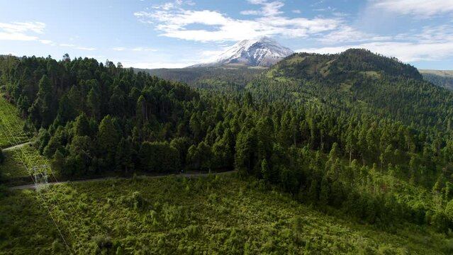 backwards drone shot dronie type showing the snowy top of the popocatepetl volcano in mexico city and the lush forests that surround it