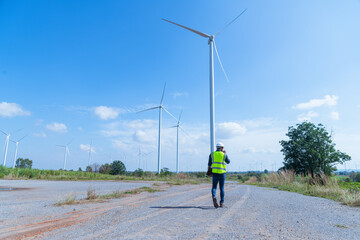 Obraz premium Engineer wearing uniform ,helmet inspection and survey work in wind turbine farms rotation to generate electricity energy. Green ecological power energy generation wind sustainable energy concept.