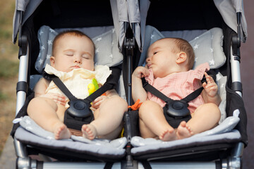 Two little twin baby girls 6 month old sleep in a double stroller on a walk outdoors