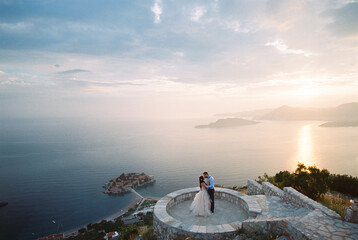 Bride and groom kiss on the observation deck over the Sveti Stefan island. Montenegro