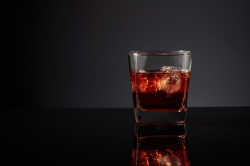 Whiskey with ice on a black reflective background.