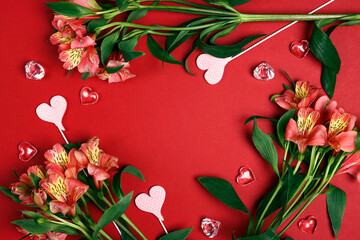 Frame of alstroemeria flowers with hearts on a red background.