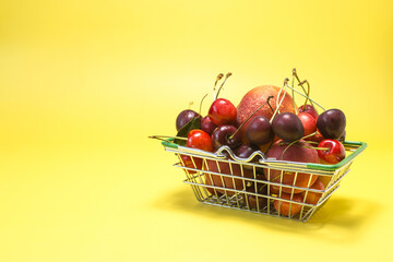 A grocery basket filled with various fruits - bananas, cherries, nectarines, apricots, peaches on a bright yellow kopi space background.