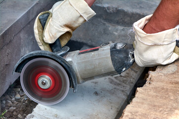 A worker with a circular saw cuts a concrete block in close-up.