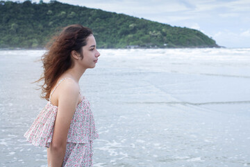 Fototapeta na wymiar Pretty teen girl walking on the beach in the morning, portrait of young teenager girl with curly hair, cloudy day by the sea