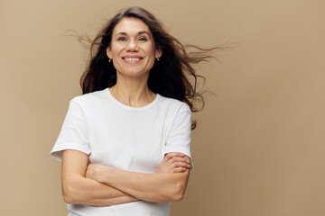 beautiful, woman with long, beautiful, well-groomed hair that develops in the wind, stands smiling sweetly at the camera, with her arms folded across her chest. Horizontal photo on a beige background.