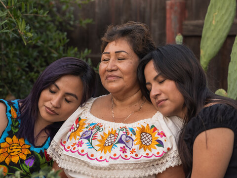 Horizontal close-up image of Indigenous women closing their eyes and standing closing together 