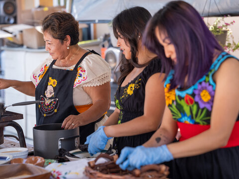Horizontal image of an Indigenous family conversing while cooking Indigenous foods 