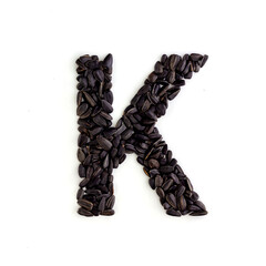 Capital letter K made from sunflower seeds. Alphabet made from sunflower seeds. White background. Sunflower seed font