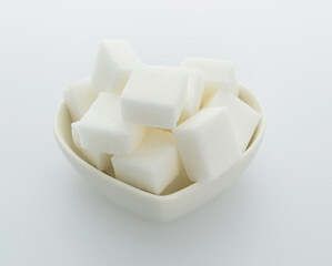 Sugar cubes in a heart shaped bowl on white background