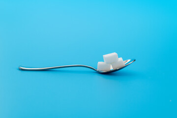Sugar cubes in a spoon on blue background