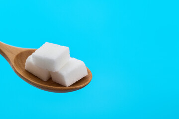 Sugar cubes in wooden spoon on blue background