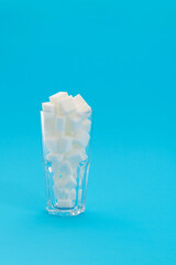 Glass cup full of sugar cubes on blue background