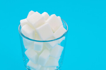 Glass cup full of sugar cubes on blue background