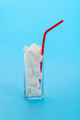 Glass cup full of sugar cubes on blue background