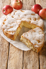 Homemade apple pie charlotte and piece of cake close-up on a parchment paper on the table. Vertical