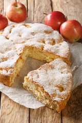 Delicious apple pie charlotte with fresh fruits and powdered sugar close-up on an old wooden table. Vertical