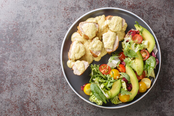 Juicy baked pork served with mustard honey sauce and lettuce, avocado and tomato salad close-up in a plate on the table. Horizontal top view from above