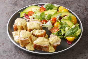 Juicy baked pork served with mustard honey sauce and lettuce, avocado and tomato salad close-up in a plate on the table. Horizontal
