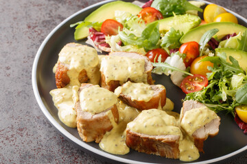 Pieces of tender pork tenderloin served with honey mustard sauce and lettuce, avocado and tomato salad close-up in a plate on the table. Horizontal