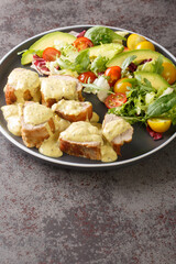 Sliced pork tenderloin served with honey mustard sauce and fresh vegetable salad close-up in a plate on the table. Vertical