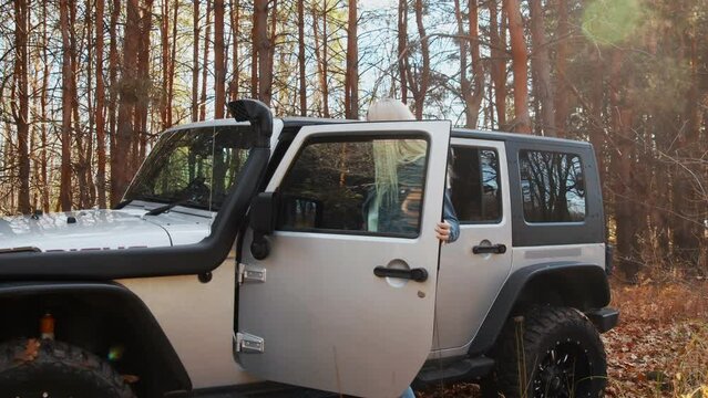 Young blonde woman sits on the passenger seat in the car jeep in autumn forest