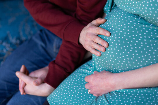 husband putting hand on pregnant wife's belly praying together