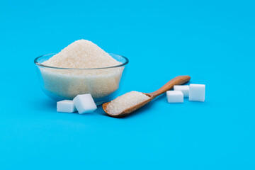 A bowl granulated sugar and sugar cubes on blue background