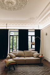 an example of a living room interior in a neo-classical style with modern elements. a sofa in the middle of a room with high ceilings and moldings.	