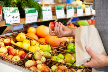 Man buying organic apples at store and putting them in paper bag