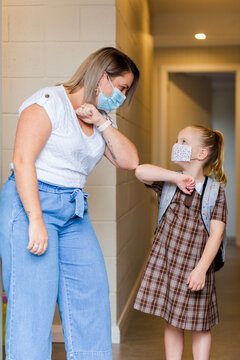 Woman In Face Mask During Covid-19 Elbow Bumping A School Child In Hallway