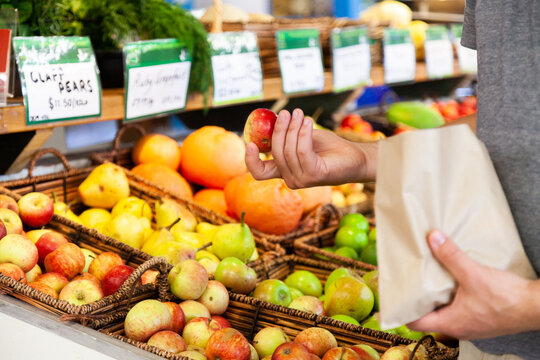 Man buying organic apples at store and putting them in paper bag