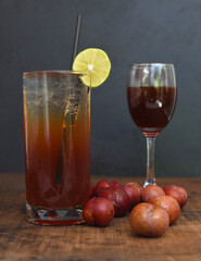 Plum wine highball cocktail with glass of wine and plums on wooden table and black background
