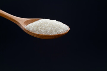 Wooden spoon with sugar crystals on black background
