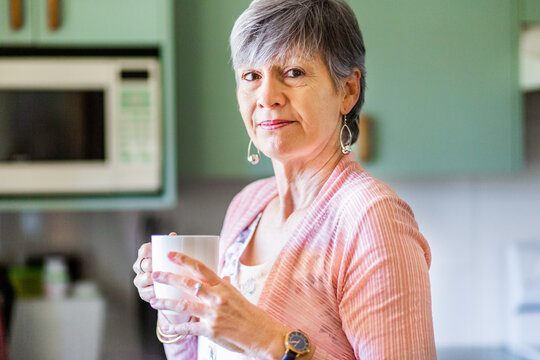 Woman with a neutral content expression standing with mug in kitchen