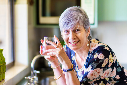 Portrait of a smiling woman drinking a glass of water in the kitchen