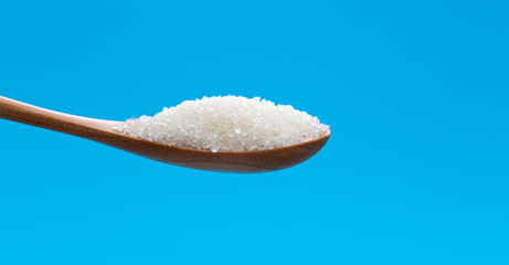 Wooden spoon with sugar crystals on blue background