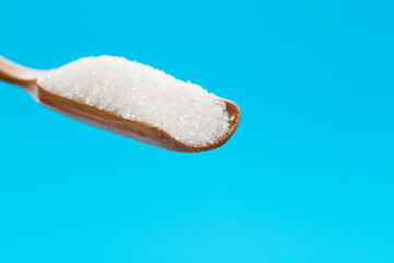 Wooden scoop with sugar crystals on blue background