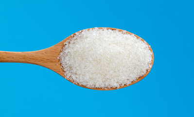 Wooden spoon with sugar crystals on blue background