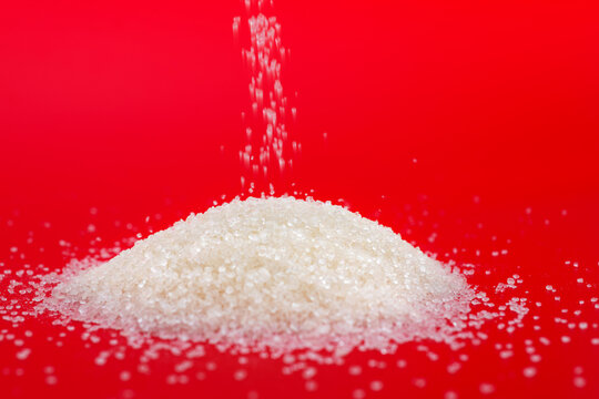 Pile of white sugar crystals on red background