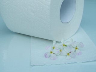 A roll of toilet paper on a white surface with white flowers on the edge of the toilet paper