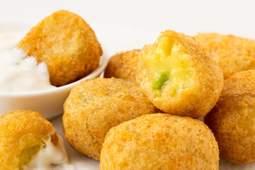 Detail of fried breaded chilli cheese nuggets next to a bowl of white sauce. One eaten.