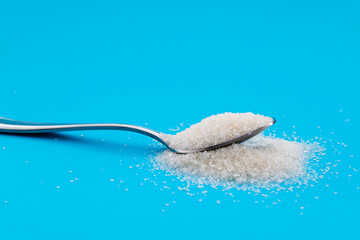Steel spoon with sugar crystals on blue background