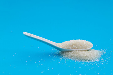 Ceramic spoon with sugar crystals on blue background
