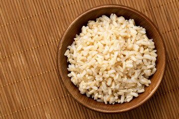Brown cooked rice in a brown wood bowl isolated on bamboo matt from above. Space for text.