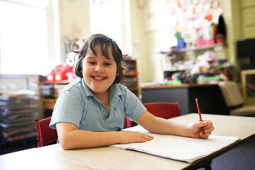 Smiling girl with short hair wearing pale blue shirt sitting and holding a pencil with a drawing pad